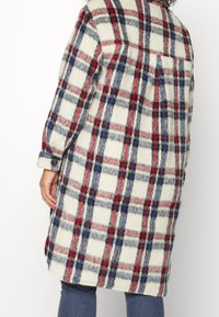 Ruudullinen villakangas takki vaaleassa, punaisessa ja sinisessä. Varustettu nappihihalla ja takataskuilla, rento muotoilu ja pehmeä rakenne.