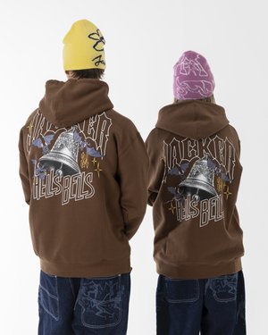 Felpa con cappuccio marrone che presenta una grafica di una campana e il testo "HELL'S BELLS", abbinata a pantaloni in denim blu. Accompagnata da berrettoni gialli e rosa.