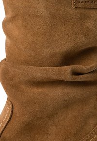 Botte en daim marron au design décontracté, avec une texture douce et des coutures visibles le long du bord. Pas de quincaillerie ou d'accents proéminents.