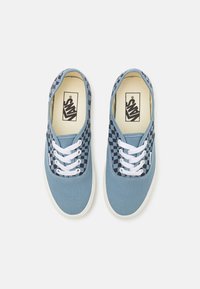 Blauwe canvas sneakers met geblokte zijpanelen, witte veters en een witte rubberen zool. Binnenin bevindt zich een zwart Vans-logo op een crèmekleurige achtergrond.