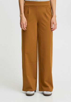 Brown wide-leg trousers made of soft fabric, featuring pleats at the waist and a relaxed fit. The hem rests above white sneakers.