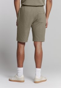 Olijfgroene katoenen shorts met zijzakken en een achterzak, omgeplooide boorden, gecombineerd met witte sokken en lichtgekleurde sneakers.