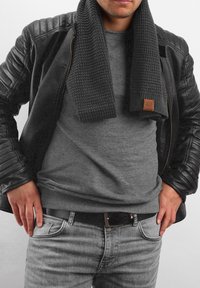 Black leather jacket with quilted shoulder detailing, gray knit scarf, gray t-shirt, and light gray jeans with a black belt.
