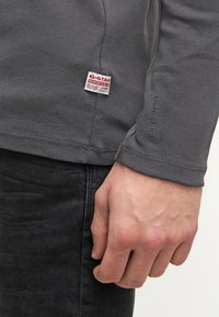 Gray long-sleeve shirt with a rounded neck, featuring a woven G-Star Originals label on the side and a textured fabric finish.