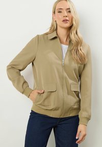 Giubbotto bomber khaki con colletto, zip frontale, polsini e orlo a costine, due tasche frontali e una texture liscia.
