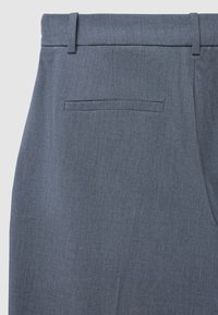 Pantaloni grigi su misura con una texture liscia, dotati di una tasca posteriore e passanti per cintura. Il tessuto presenta un sottile motivo a intreccio.