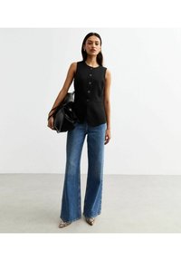 Svart ärmlös väst med framknappar och två fickor, matchat med flare jeans i blått. Tillbehör inkluderar en stor svart väska.