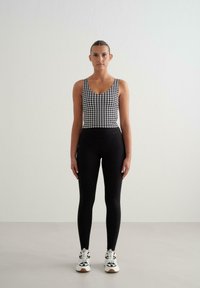 Juodos leggingai derinami su be rankovių juodai baltu šuniuko danties raštuotu marškinėliu, papildyti baltais sportiniais bateliais su juodais akcentais.