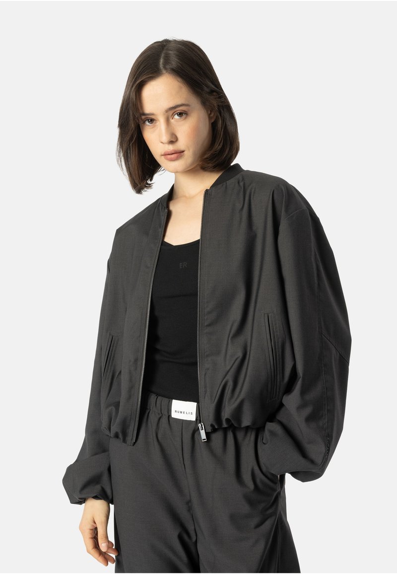 Czarna kurtka bomberka z zamkiem z przodu, elastycznymi mankietami i bocznymi kieszeniami, wykonana z gładkiego materiału i w luźnym kroju, stylizowana z pasującymi spodniami.