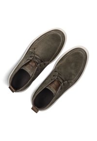 Olijfgroene suède schoenen met witte rubberen zolen, bruine leren accenten, ronde neus en traditionele veters. Geen zichtbare patronen.