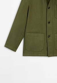 Veste à manches longues vert olive avec fermeture à boutons sur le devant et deux grandes poches plaquées carrées sur fond blanc.