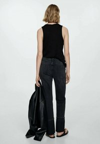 Black tank top and high-waisted black denim jeans, featuring a straight cut and slightly flared hems, held next to a black leather jacket.