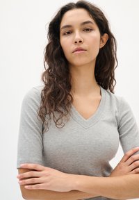 Szürke bordázott kötött rövidujjú felső, V-nyakkal és testhez simuló fazonnal. Simább textúrájú, enyhén rugalmas anyag a kényelem és a modern megjelenés érdekében.