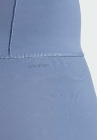 Een blauw sportmateriaal met een gladde textuur, met een zichtbare naad en het reliëfwoord "AEROREADY" nabij de onderrand.