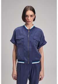 Mörkblå bombarjacka med kort ärm som har dragkedja framtill, två bröstfickor och randiga ribbade detaljer vid kragen och nederkanten.