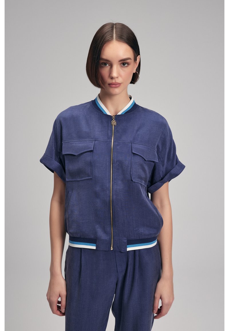 Mörkblå bombarjacka med kort ärm som har dragkedja framtill, två bröstfickor och randiga ribbade detaljer vid kragen och nederkanten.