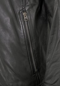 Schwarze Lederjacke mit glatter Textur, ausgestattet mit einem silbernen Reißverschluss an der Seite zur Schließung und mit Details an den Nähten.