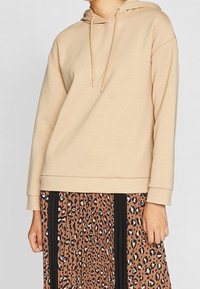 Hoodie beige in tessuto morbido con cappuccio regolabile e vestibilità comoda, abbinato a una gonna plissettata con una stampa leopardata marrone e nera.