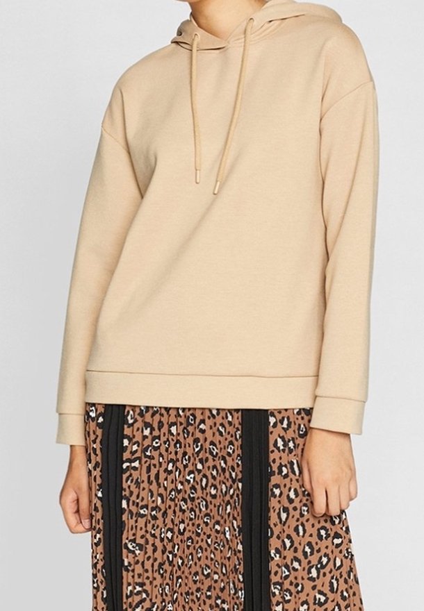 Hoodie beige in tessuto morbido con cappuccio regolabile e vestibilità comoda, abbinato a una gonna plissettata con una stampa leopardata marrone e nera.