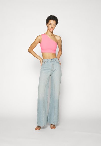 En-erkjole i hot pink med én skulder, kombinert med lyseblå vide jeans. Materialet er glatt; jeansene har høy midje og løs passform.