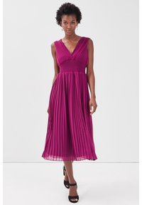 Un vestido acampanado de longitud a la rodilla en fucsia con escote en V y corsé ajustado, que presenta una cintura fruncida y una falda fluida. Sandalias de tacón negro.