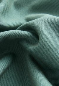 Tissu en coton de couleur verte douce, avec une texture lisse, un motif de tissage diagonal et des plis délicats.