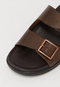 Smeđi kožni sandal s dva široka remena, kopčom boje bakra i teksturiranim crnim uloškom s fleksibilnom gumenom potplatom.