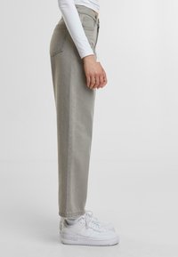 Pantalones ajustados de pierna recta en gris claro con cintura alta, fabricados en denim, que cuentan con bolsillos laterales y traseros. Combinados con zapatillas blancas.