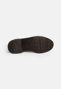 Semelle de chaussure noire avec surface texturée, dotée de clous ronds pour une meilleure adhérence et d'une zone lisse près du talon. Design plat et de forme ovale.