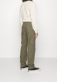 Olijfgroene cargobroeken van katoen, met meerdere zakken en een rechte pasvorm. Gecombineerd met een lichtgekleurde lange mouwen shirt en sneakers.