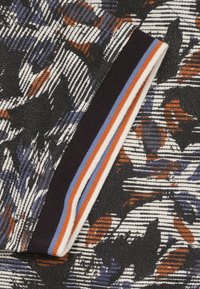 Gebreide stof met een zwarte achtergrond en meerkleurige bloemmotieven in paars, oranje en wit, afgewerkt met een gestreepte ribbelrand.