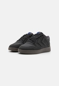 Czarne sneakersy ze gładką skórzaną cholewką, zaokrąglonym noskiem, perforowanym wzorem, teksturą w kropki i szarym gumowym podeszwa; zawierają niebieskie akcenty na języku.