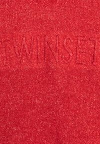 Czerwony, dziany materiał z subtelnym wytłoczonym tekstem "TWINSFT", zlewającym się z fakturą.