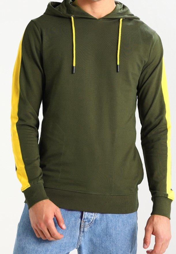 Uomo che indossa un felpa con cappuccio verde oliva, con stringhe gialle e strisce gialle lungo le maniche, abbinato a jeans azzurri chiari.