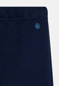 Mørkeblå bomullsblanding stoff med en glatt tekstur og et elastisk liv. Lite blått logo-preg nær livet.