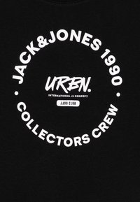 Fekete pamut póló, fehér kör alakú felirattal: "JACK & JONES 1990 URBN. COLLECTORS CREW JJ90 CLUB" vastag tipográfiával.