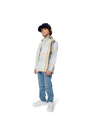 Lichtblauw en geel geruite blouse, gelaagd over een wit T-shirt, gecombineerd met blauwe jeans en witte sneakers; marineblauwe pet.