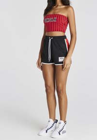 Top de tubo a rayas rojas con letras negras, combinado con pantalones cortos negros con paneles laterales rojos, detalles en blanco y parche con logo. Zapatillas blancas.