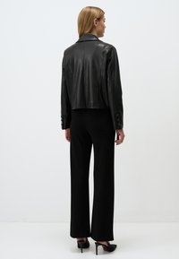 Korte zwarte leren jas met een puntige kraag, een gladde textuur en knopenaccenten; gecombineerd met high-waisted zwarte broeken en hakken.