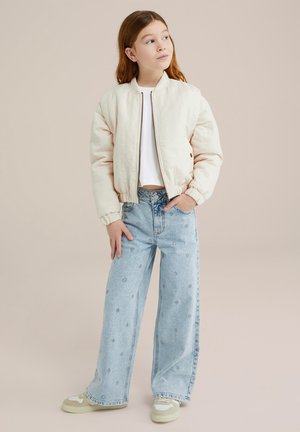 Lightly padded cream bomber jacket with a front zipper, paired with high-waisted blue jeans featuring floral embroidery. Cream and green sneakers.