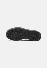 Black rubber shoe sole featuring a textured pattern with circular and arrow motifs for enhanced grip and traction.