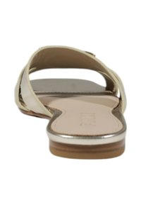 Sandalias planas con un empeine sintético color crema, acentos metálicos plateados y una suela inferior de color marrón claro. Diseño de punta abierta con soporte de arco mínimo.