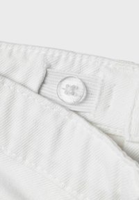 Tissu en denim blanc avec un bouton clair et une boutonnière plate. Surface texturée avec des coutures visibles le long des bords.