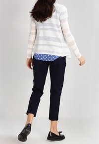 Vit och ljusblå randig stickad kofta lagd över en blå prickig skjorta med marinstickade byxor och svarta platta skor, sedd bakifrån.