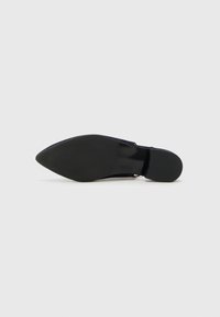 Chaussure noire à bout pointu avec une tige en daim lisse, présentant une accent en vinyle et une semelle en caoutchouc texturée pour une meilleure adhérence.