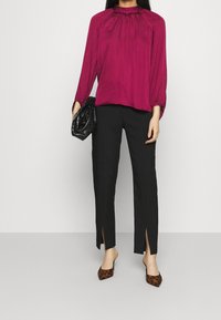 Blusa di raso fucsia con maniche lunghe, scollo arricciato, abbinata a pantaloni neri tailorati con spacchi laterali e tacchi con stampa animale.