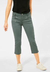 Gröna cropped byxor med slim fit, med två framfickor och en dragkedjedetalj på ena sidan, tillverkade av ett mjukt, stretchigt material.