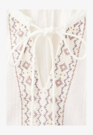 Bijela bluza s V-izrezom ukrašena složenim vezom u svijetlo smeđoj i mauve boji, naglašena malim perlicama i vezicama na izrezu.