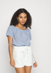 Blusa azul e branca em riscas com mangas curtas e decote elástico, combinada com calções brancos de cintura alta com laço e detalhes em ilhós.