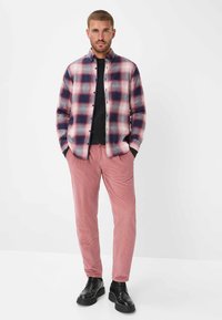 Gekleed ruitenhemd in rood, blauw en wit, gecombineerd met corduroy broek in lichtroze. Zwarte schoenen, slank fit ontwerp.